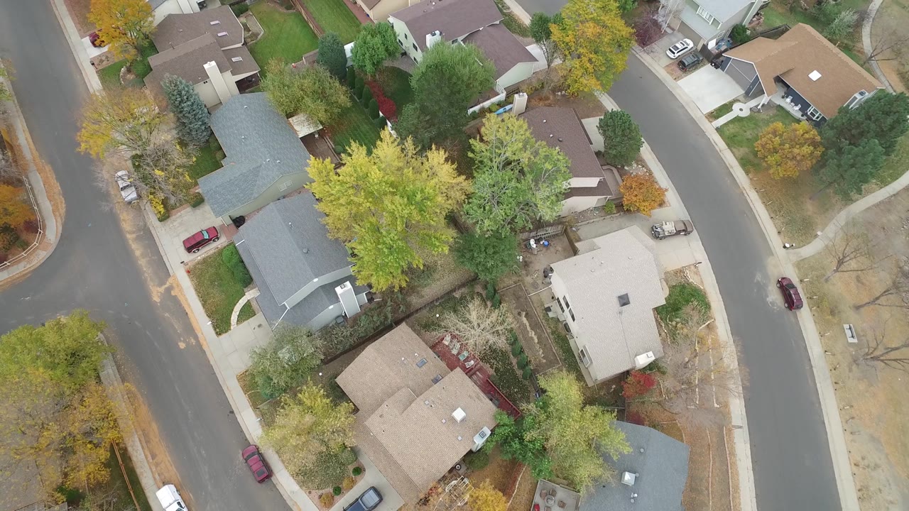 Aerial frame over Hidden Lake, Colorado with gray and tan rooftops, residential lawns, a curved street, parked cars, and no visible people.
