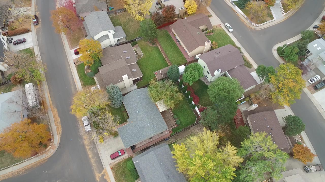 Overhead view of houses, lawns, streets, and autumn trees.