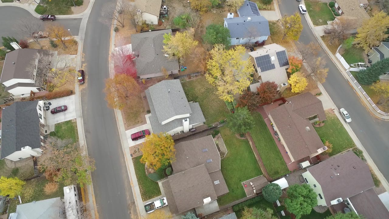 Overhead view of houses, streets, cars, lawns, and autumn trees.