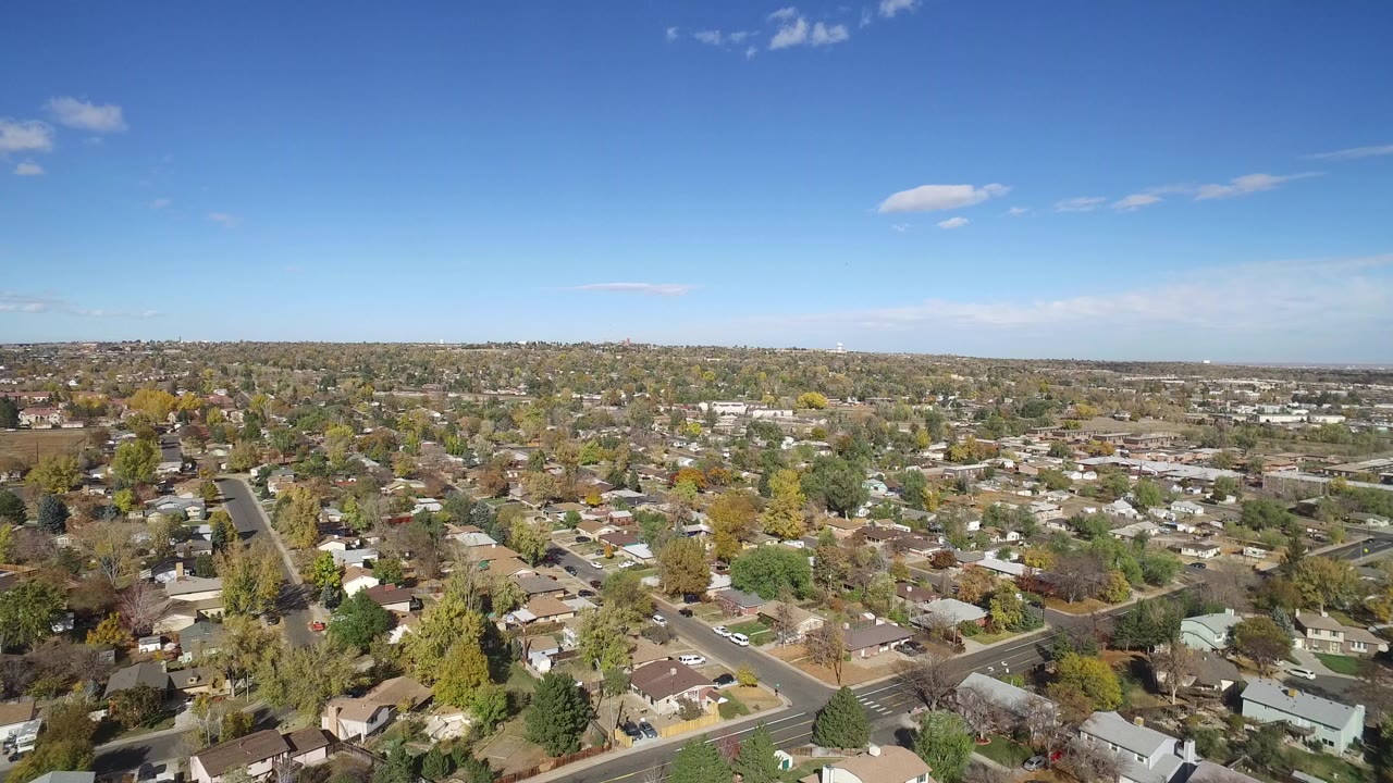 Wide aerial view over Hidden Lake, Colorado homes, street grids, fall-colored trees, and a clear blue sky at the start of the clip, with no visible people.