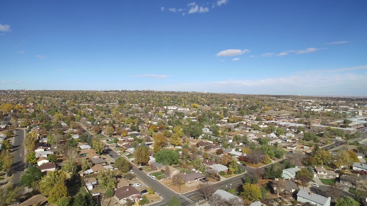 Aerial view over suburban homes and tree-lined streets under a blue sky.