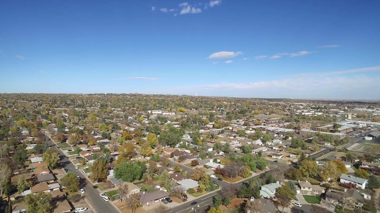 Aerial frame over Hidden Lake, Colorado, with more of the neighborhood grid visible below a level horizon and small clouds in the blue sky.