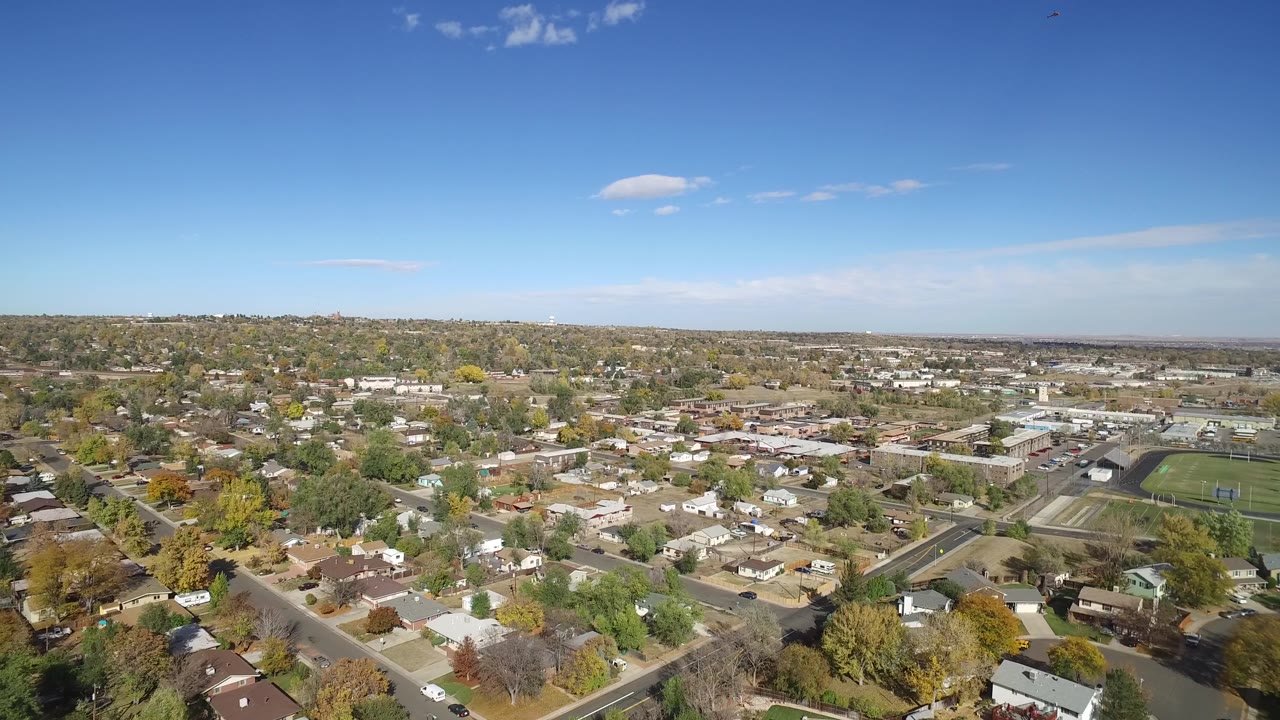 Aerial view of homes, streets, trees, and a sports field under blue sky.