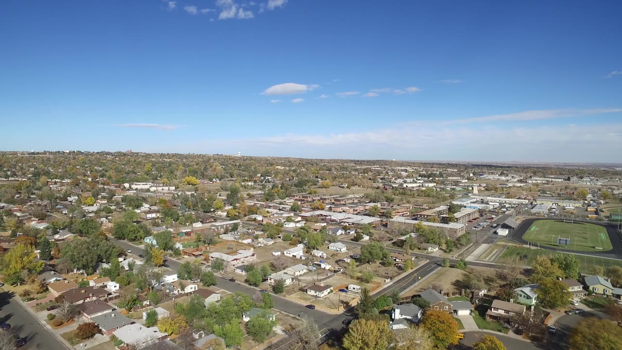 Second aerial frame in Hidden Lake, Colorado, showing rooftops across the foreground, a road grid through the center, a green athletic field on the right, and no visible people.