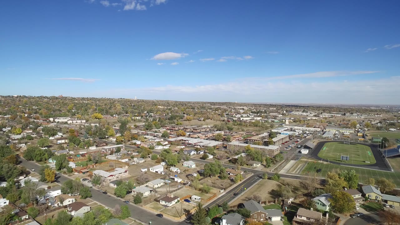 Aerial view of homes, streets, open lots, and a sports field under blue sky.