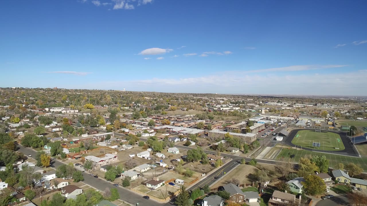 Hidden Lake, Colorado residential blocks stretch across the frame, with open land in the foreground, a school-like sports field to the right, and no visible people.