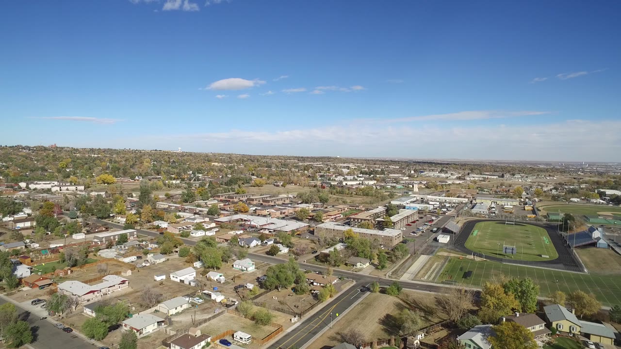 Aerial view of homes, roads, and a green athletic field under a blue sky.