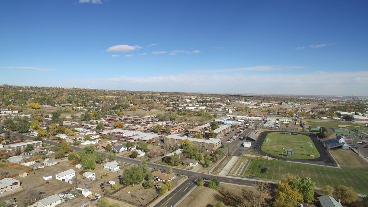 Aerial view over suburban streets, homes, and athletic fields under blue sky.