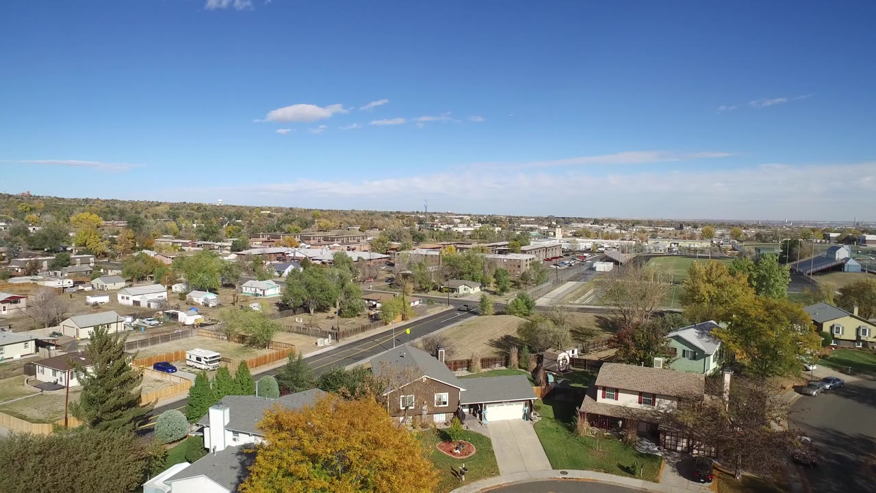 Elevated view over suburban houses, streets, trees, and blue sky.