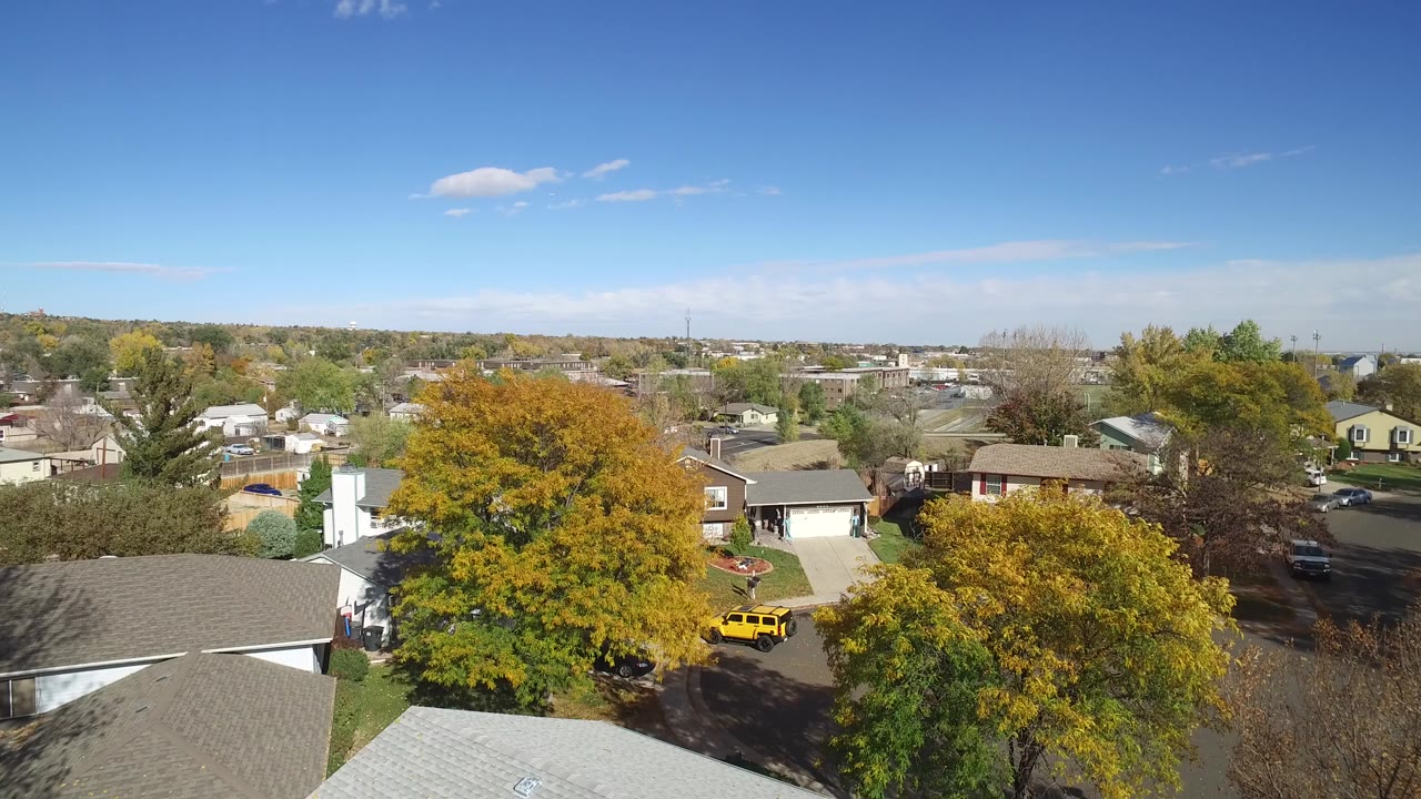Aerial view over rooftops, autumn trees, and a residential street