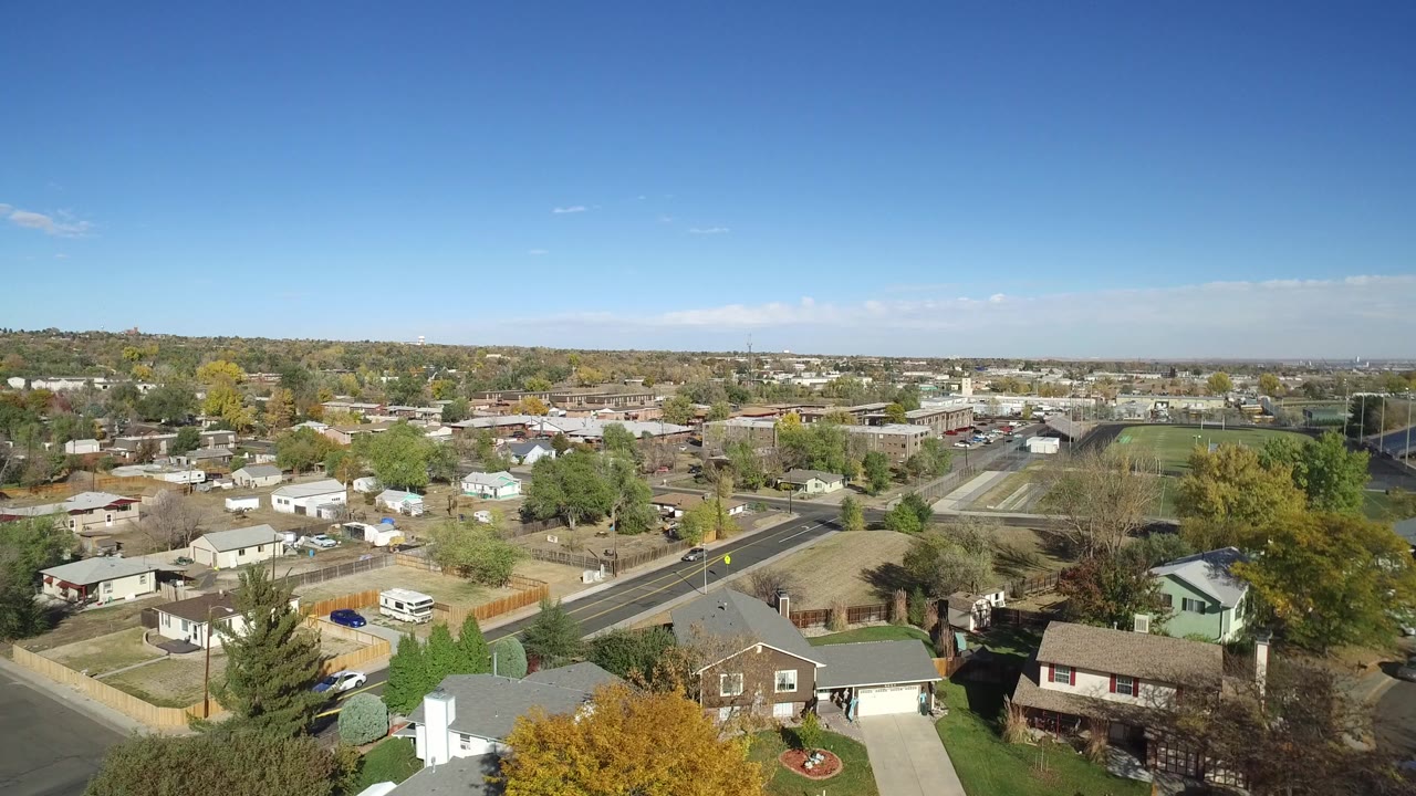 Second frame holds a high view across Hidden Lake, Colorado, showing more of the residential blocks, a curving road, scattered vehicles, distant hills, and no visible people.