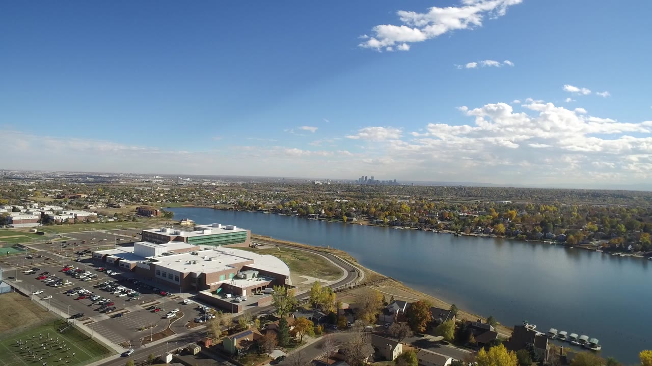 Hidden Lake, Colorado aerial view with the low waterfront building lower left, the lake across the middle, neighborhoods beyond, and the skyline faint on the horizon.