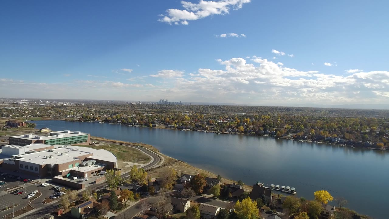 Drone-height view across water toward trees and a distant city skyline