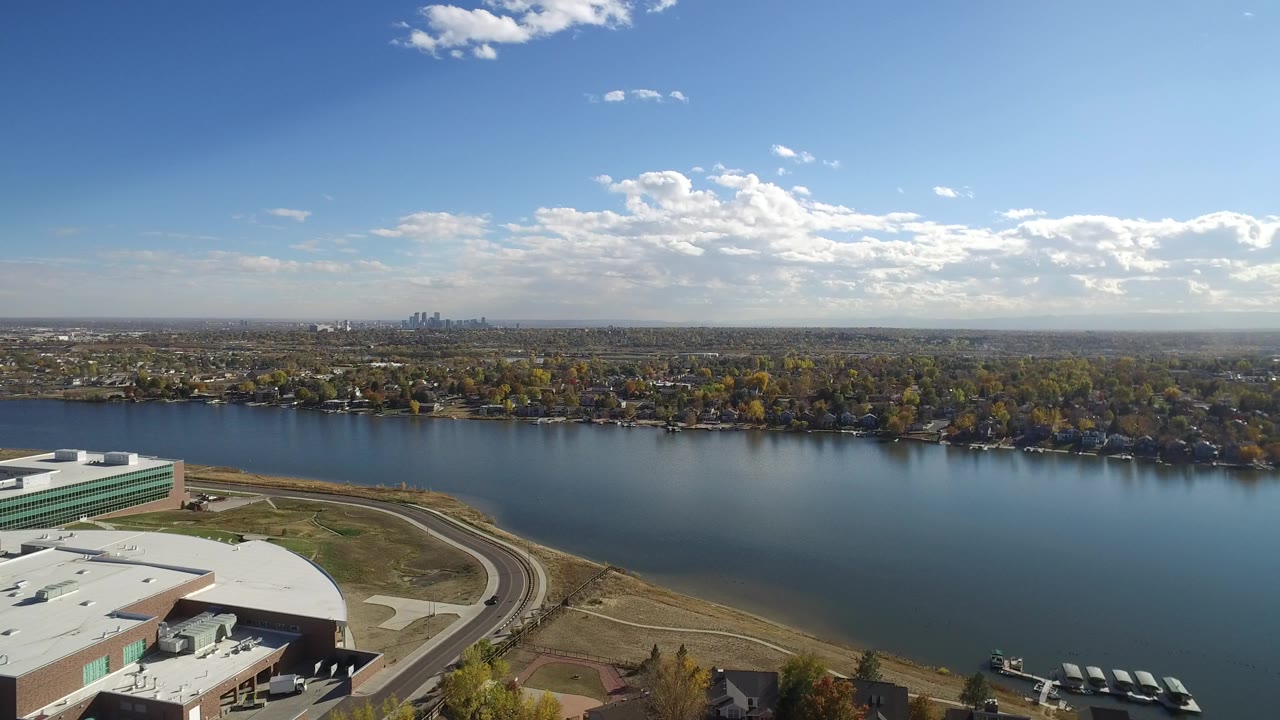 Aerial view of a broad waterway, curved road, large roof, trees, and distant skyline.