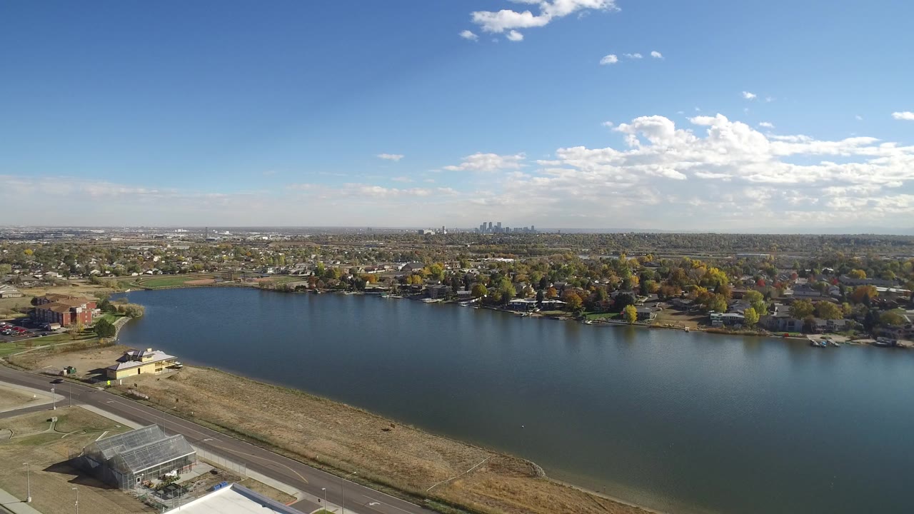 Aerial view of a lake with dry shoreline, roads, houses, trees, and distant skyline.
