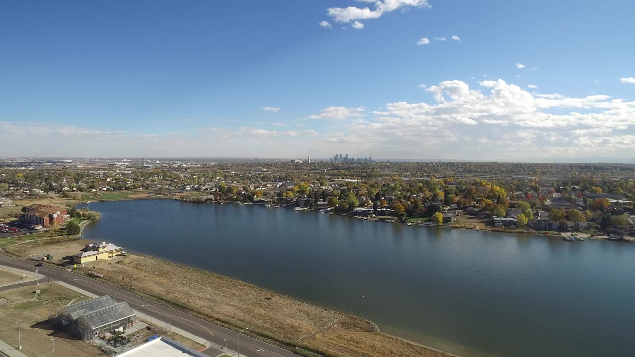 Aerial view in Hidden Lake, Colorado with the lake centered, dry foreground land, a road at lower left, houses and trees across the water, distant skyline, and no visible people.