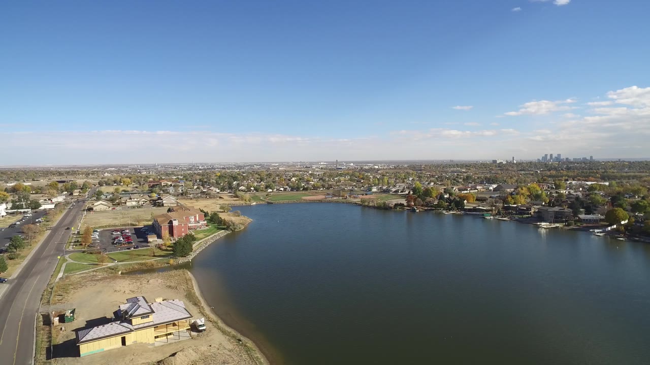 Aerial view over Hidden Lake, Colorado, with the road and dry shoreline in the foreground, open water filling the center, homes around the far bank, and no visible people.