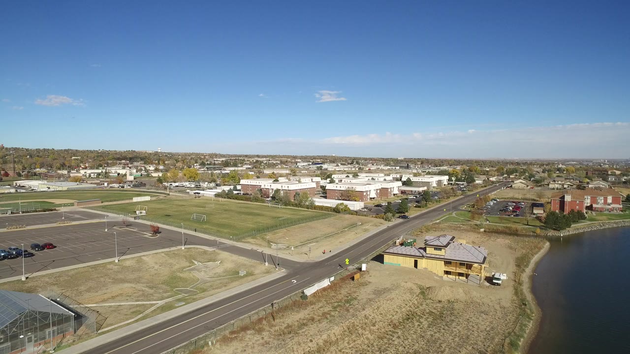Aerial view of roads, fields, buildings, and a lake edge under clear sky.