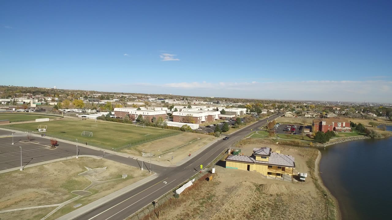 Aerial view of a lake, road intersection, fields, and low buildings.
