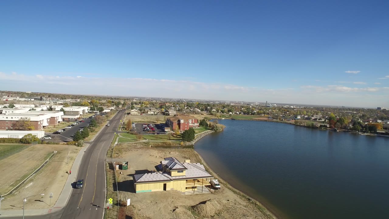 Drone view of a road beside a large lake with town buildings in the distance.