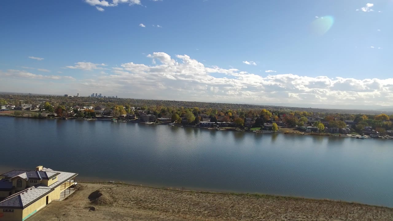 Wide elevated view across water with a house on the near bank and homes beyond.