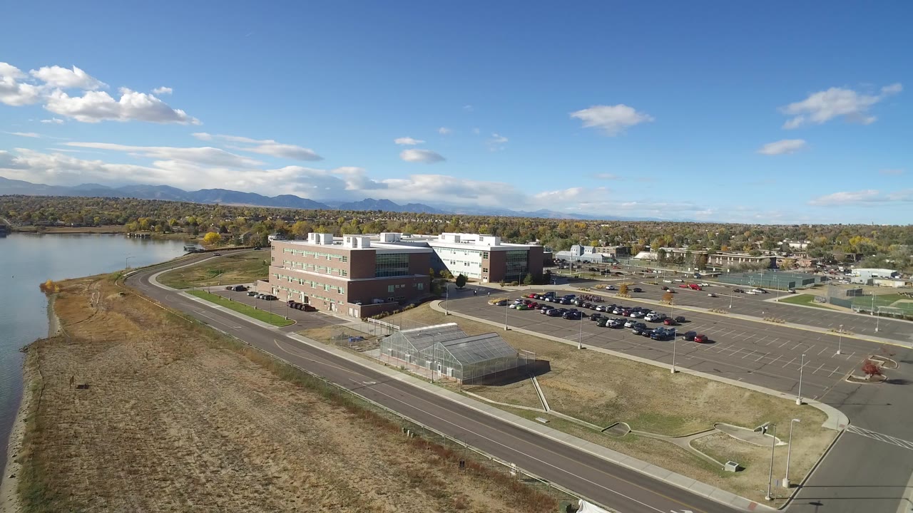 Drone view of a parking lot, buildings, road, lake edge, and mountains.