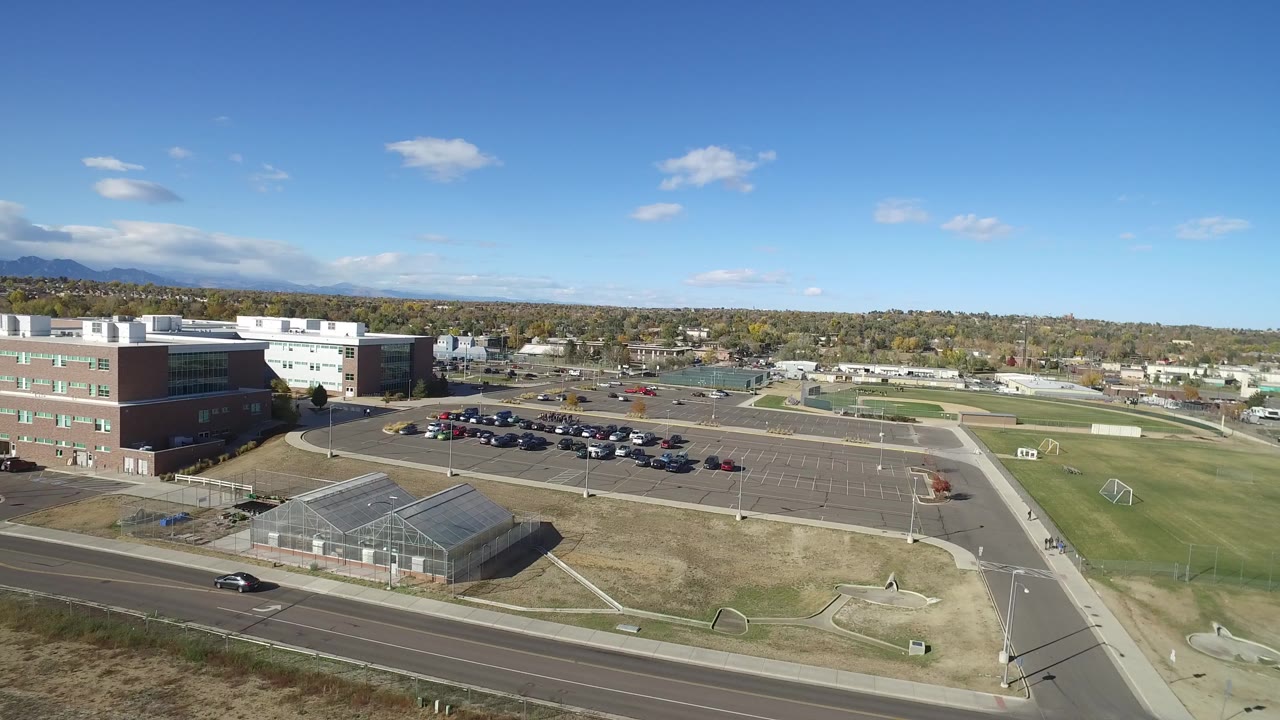Elevated suburban view with buildings, parking lot, road, fields, and blue sky.