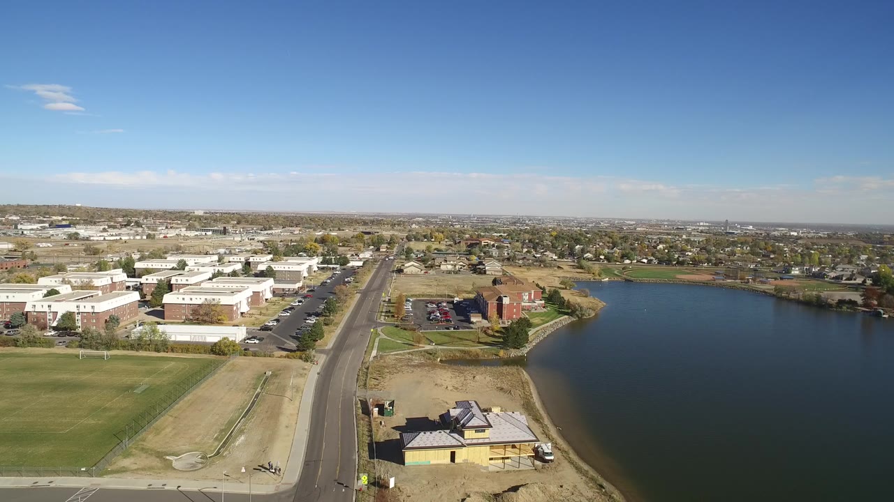 Opening aerial frame over Hidden Lake, Colorado, showing a road along the water, low buildings, dry grass lots, distant homes, and no visible people.
