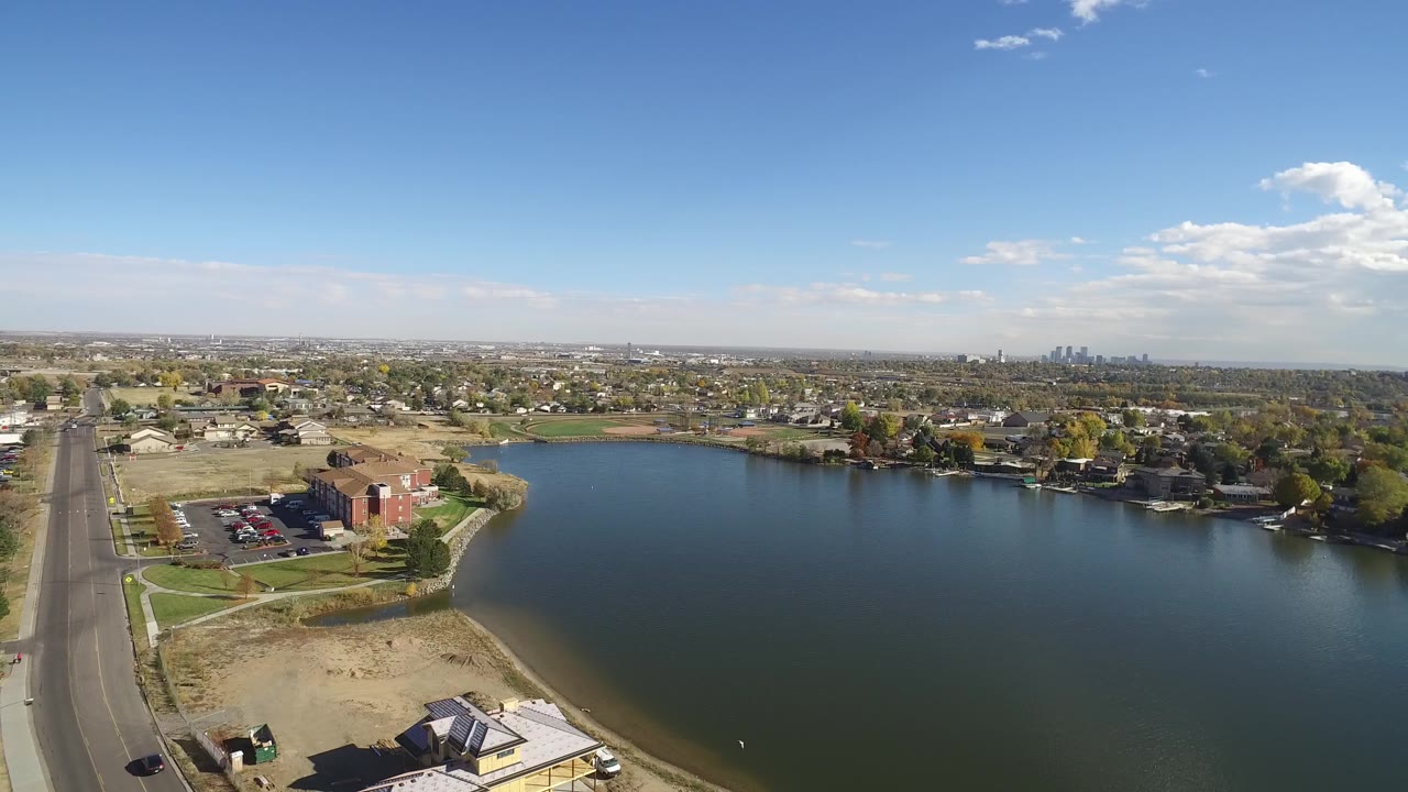 Aerial view over a lake with shoreline, road, homes, and distant skyline.