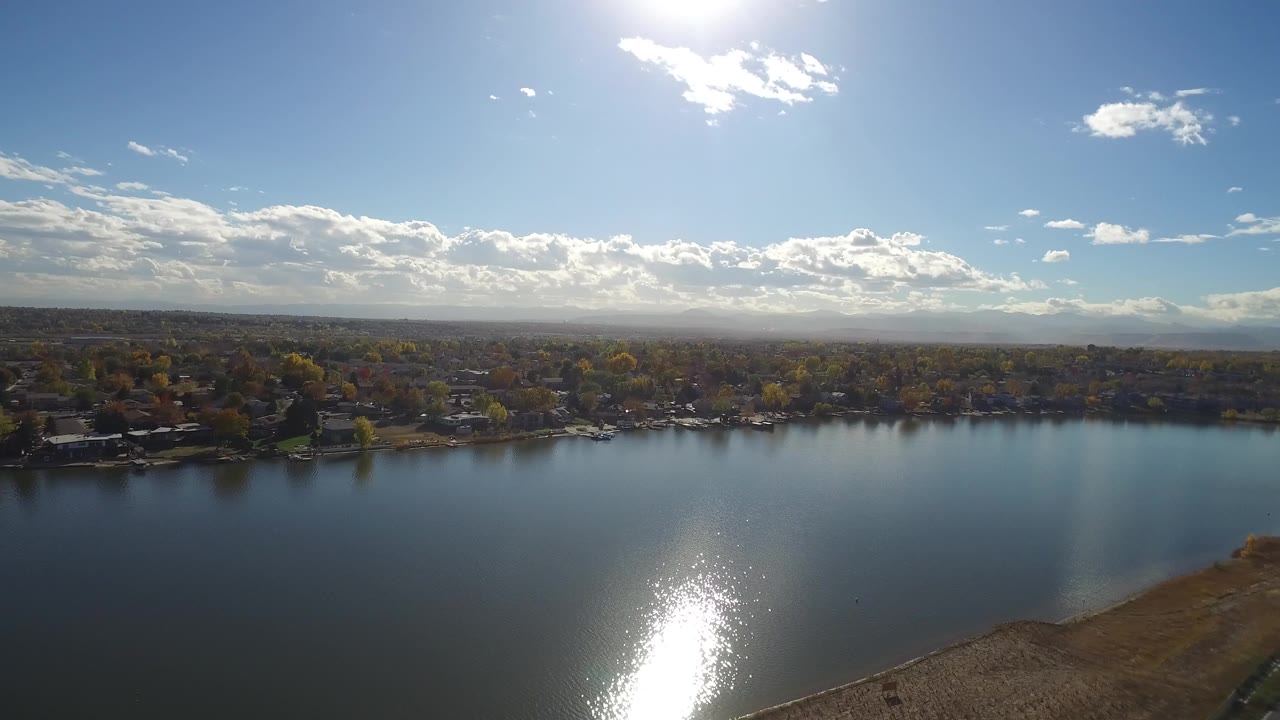 Wide aerial view over a lake with sun glare and a tree-lined shoreline.