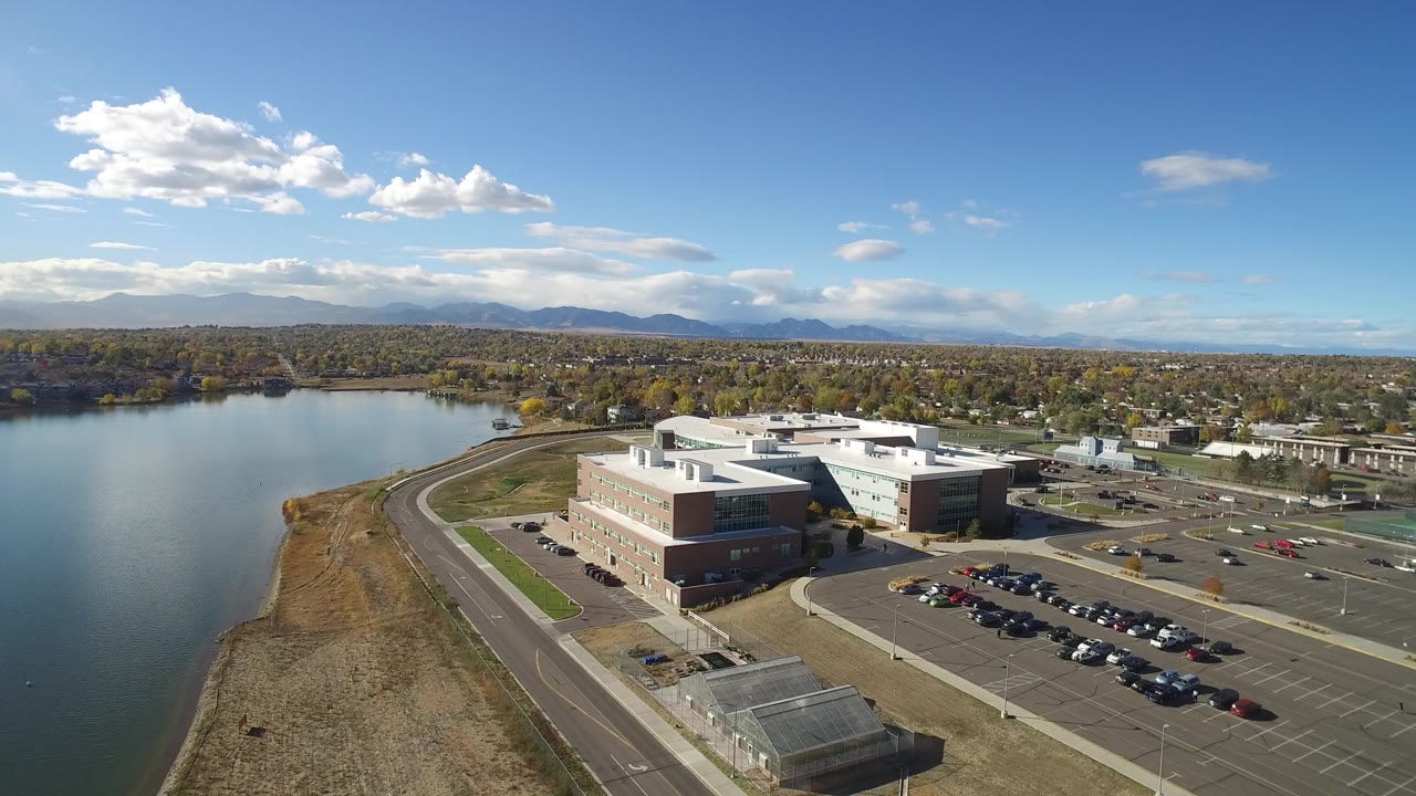 Aerial view of a large building complex beside a lake and parking lots.