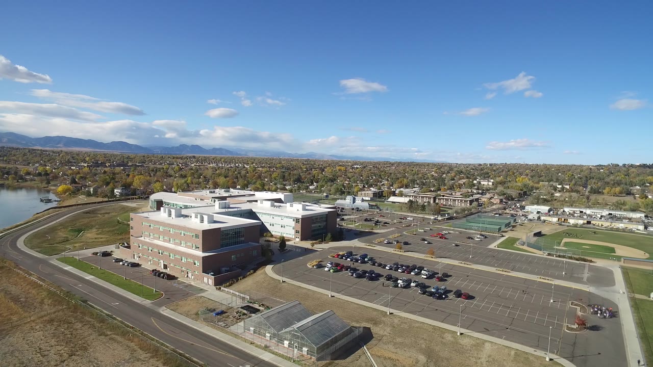 Aerial view of a large building complex, parking lot, roads, fields, and distant mountains.