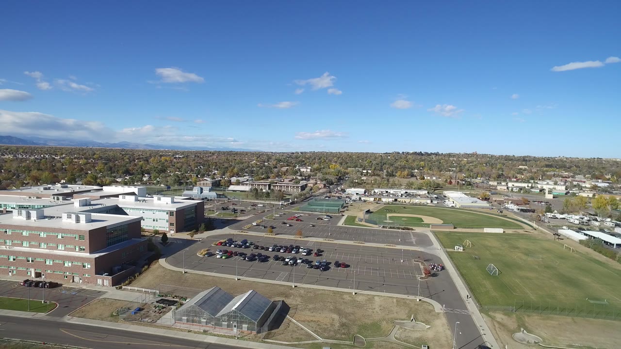 Aerial view of campus buildings, parking lots, fields, and distant neighborhoods under a blue sky.