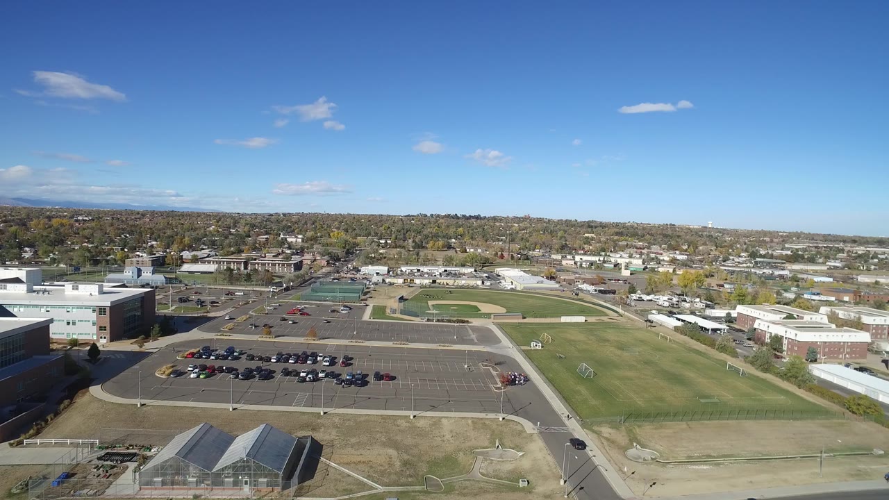 Aerial view in Hidden Lake, Colorado with the baseball diamond and green field centered beyond a parking lot, with low buildings and no visible people.
