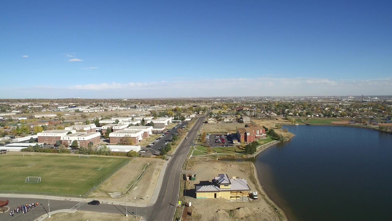 Aerial view of a lake beside a road, buildings, and a grass field.