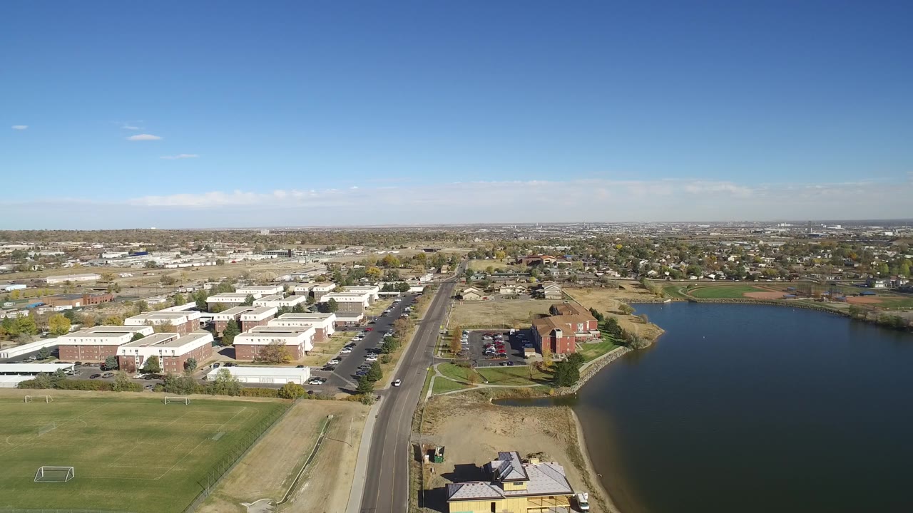 Drone-like view of a lake, roadway, buildings, and fields.
