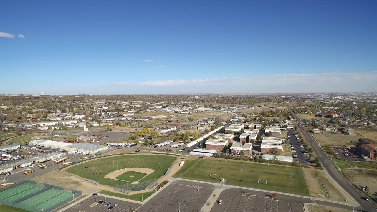 Aerial view of baseball field, tennis courts, roads, and suburban blocks.