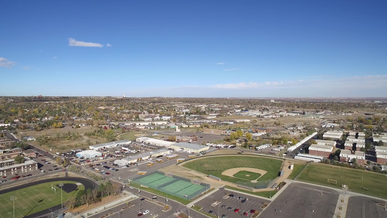 Second aerial frame over Hidden Lake, Colorado, with the baseball diamond near center, green courts at lower left, school-like buildings, parking lots, roads, and no visible people.