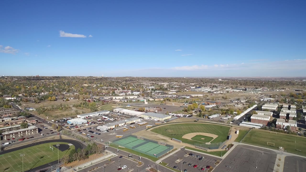 High drone view of a baseball field, track, courts, streets, and distant neighborhoods.
