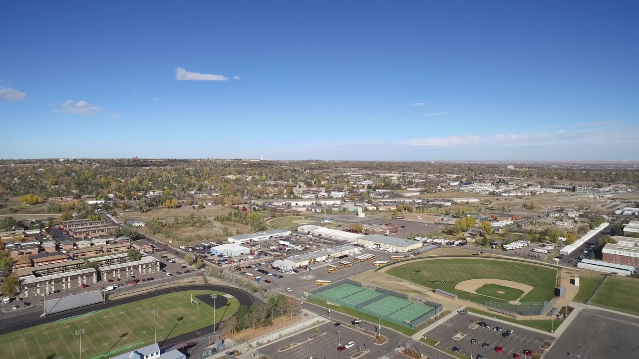 Aerial view of sports fields, tennis courts, streets, and low buildings under a blue sky.