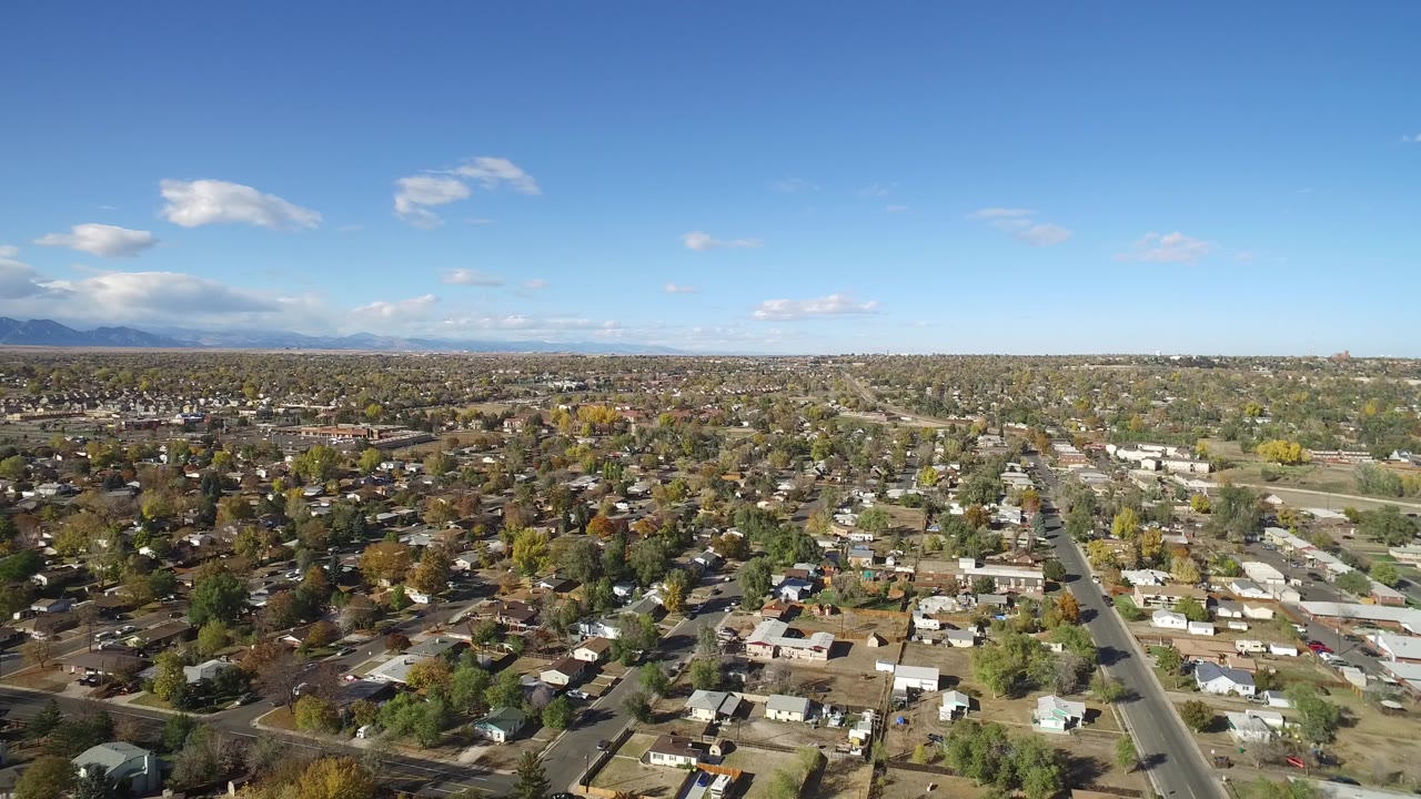 Second aerial frame over Hidden Lake, Colorado showing a dense spread of rooftops, tree cover, long roads, mountain backdrop, and no visible people.
