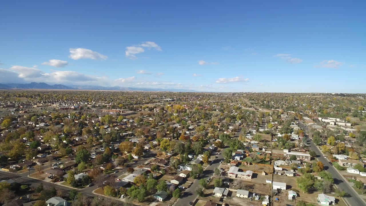 High aerial view over Hidden Lake, Colorado homes and streets with distant mountains under scattered clouds, with no recognizable people visible.