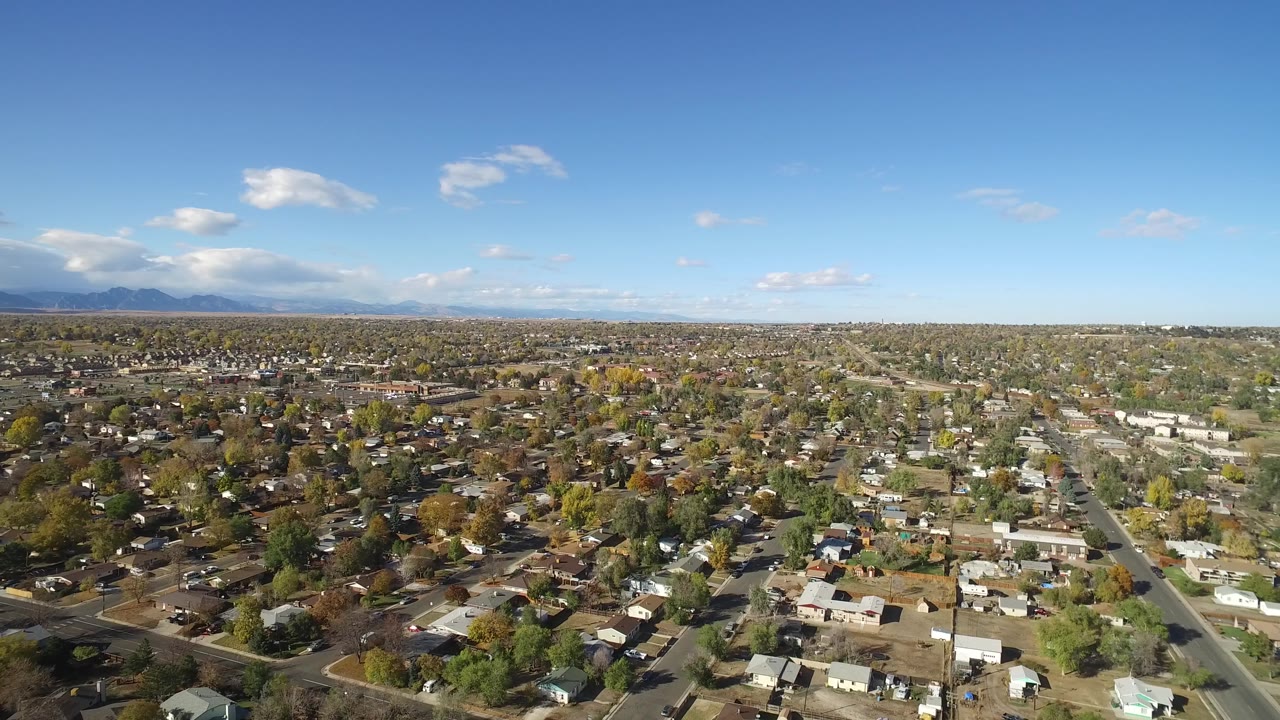 Elevated view across Hidden Lake, Colorado rooftops and tree-lined blocks, with the mountain range low on the left horizon and no recognizable people visible.