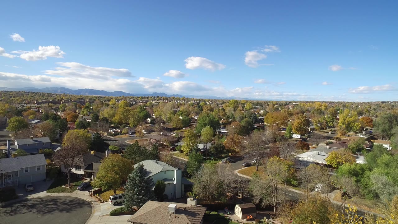 Elevated daylight view across Hidden Lake Colorado homes, mixed autumn trees, curved residential streets, blue sky, distant mountains, and no visible people.