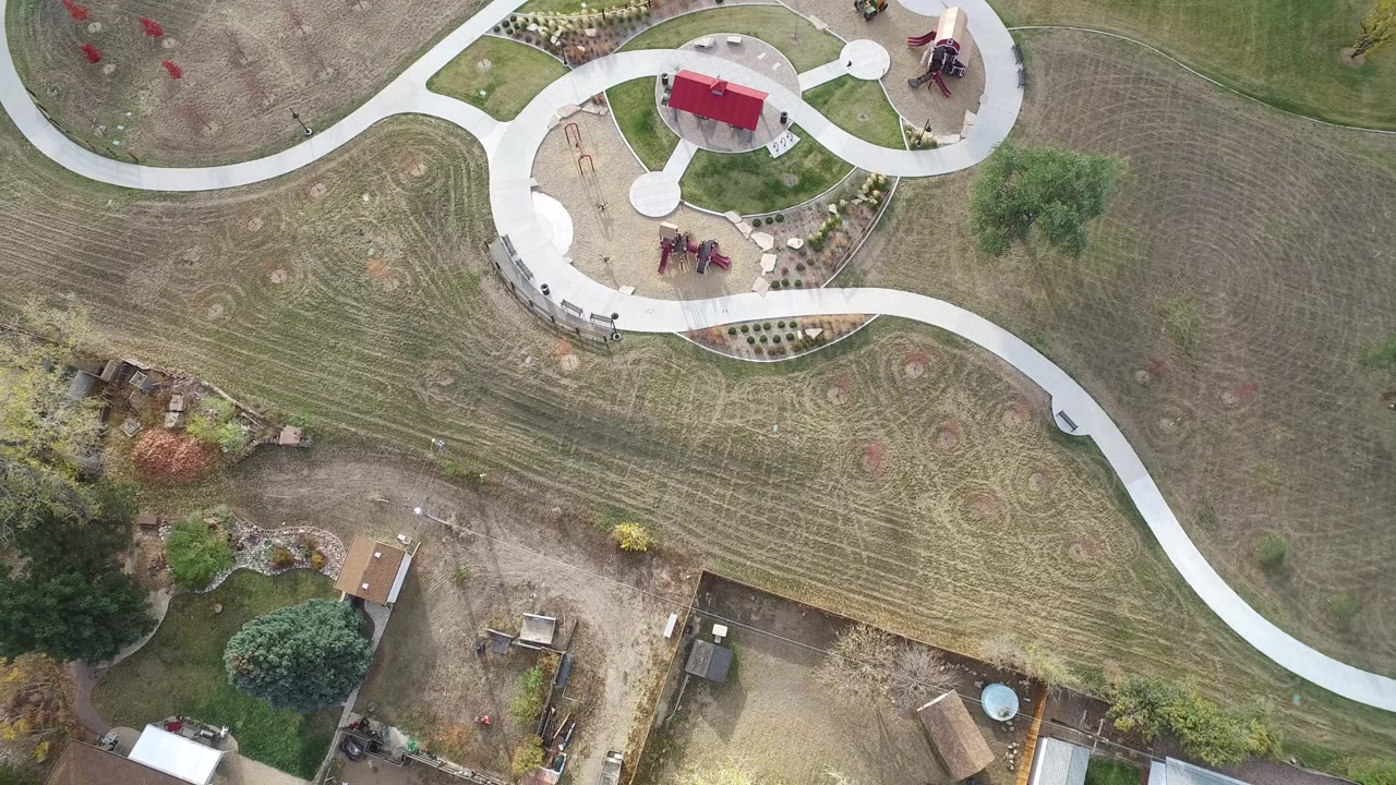 Top-down neighborhood park view with curved concrete paths and surrounding rural yards.