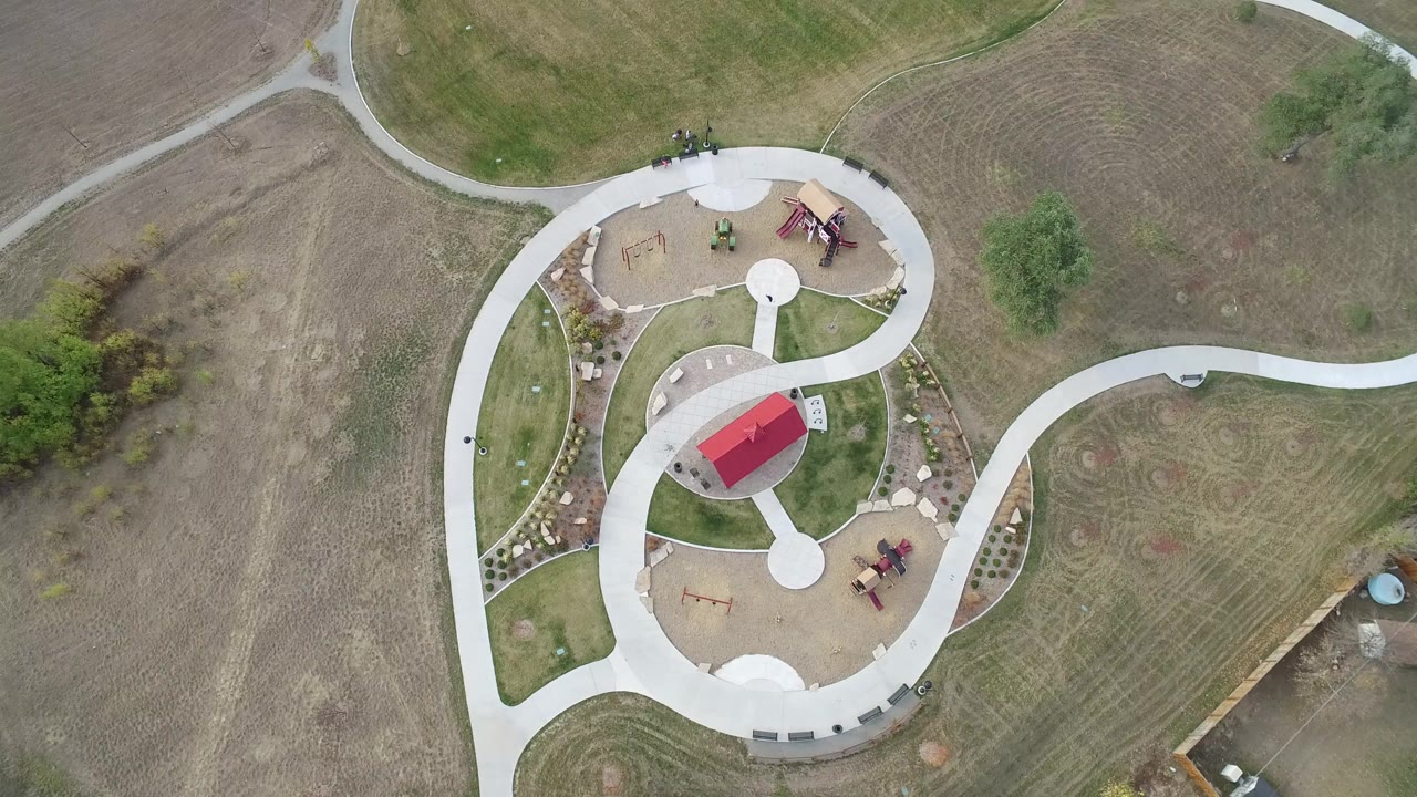 Overhead aerial frame of a Hidden Lake, Colorado park with a red-roofed shelter, circular paths, tan play areas, grass, and no visible people.