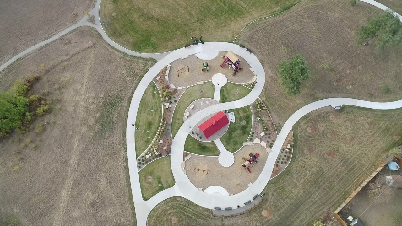 Aerial view over Hidden Lake, Colorado showing the red-roofed park shelter, circular walkway connections, bare open ground, grass, and no visible people.