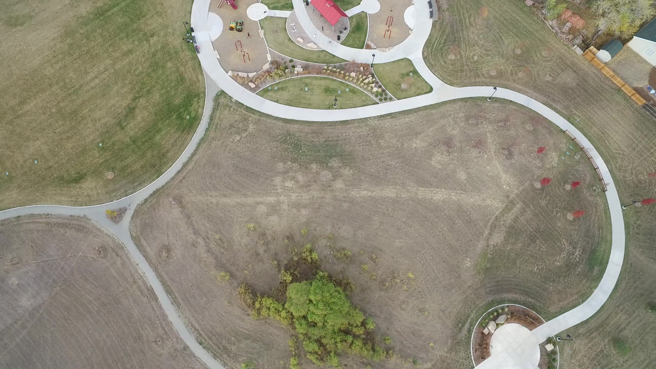 Overhead Hidden Lake, Colorado view with the path network crossing mowed grass, a partial red-roofed structure or play area at the top edge, trees near the lower edge, and no visible people.