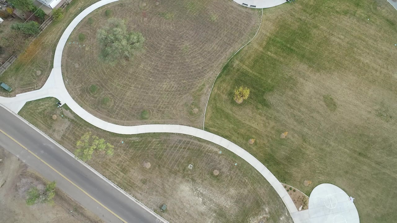Aerial view of curving sidewalk, open lawn, and road below.