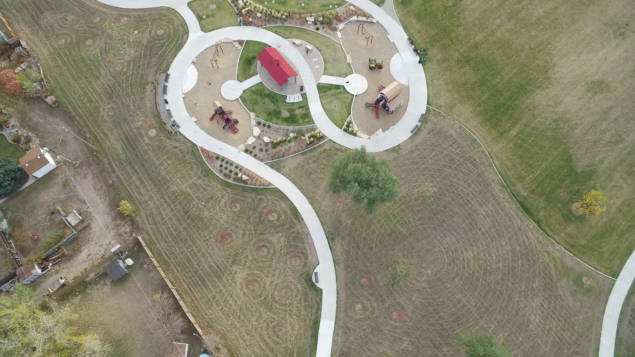 Overhead view of curved park paths, lawns, play areas, and nearby construction lots.
